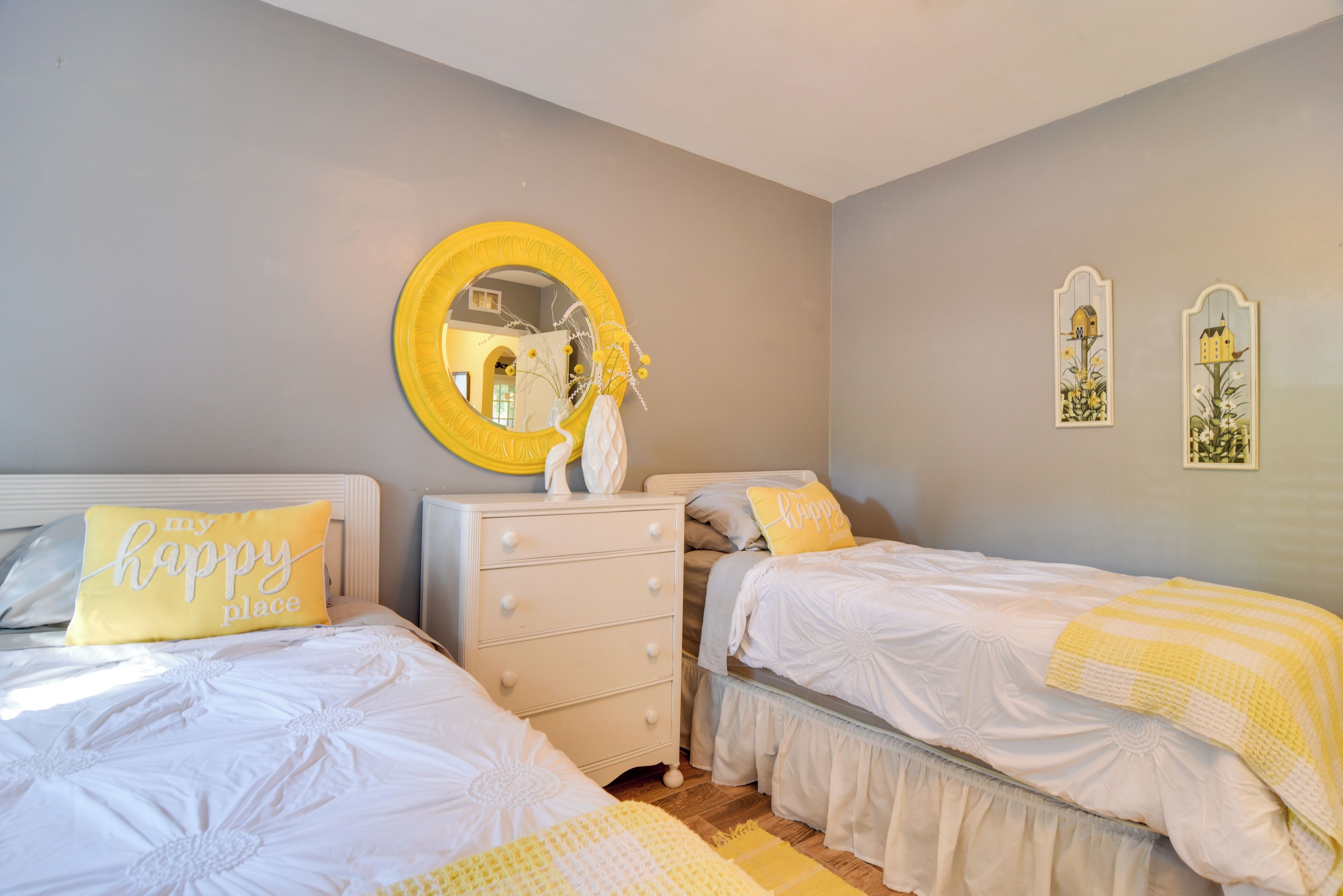 A bedroom with two beds, a dresser, a mirror, and decorative wall art.