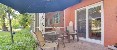 Un patio al aire libre con una mesa, sillas, un paraguas azul y piso de ladrillo.
