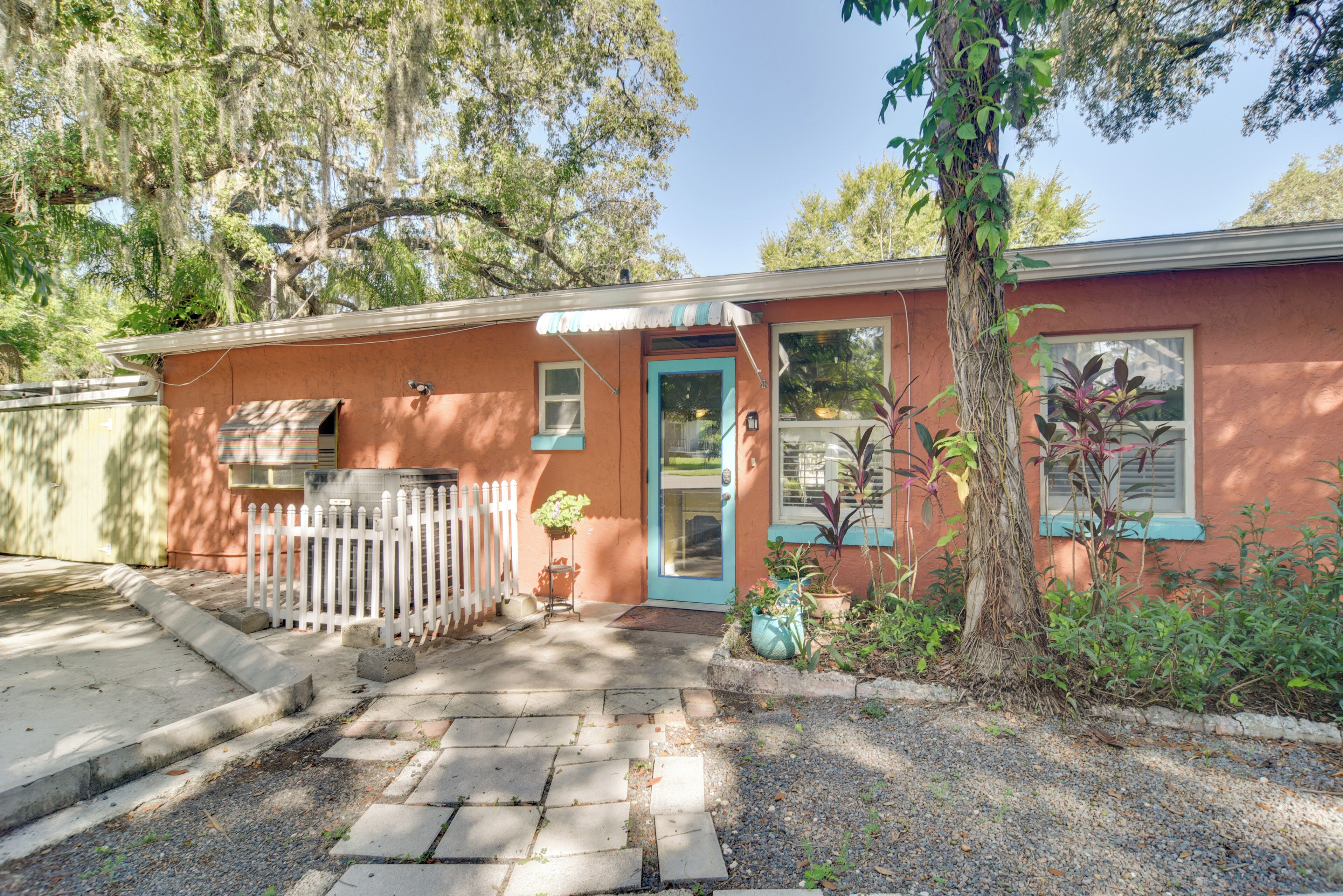 A single-story building with a red exterior, a blue door, and a small porch area with a white picket fence.