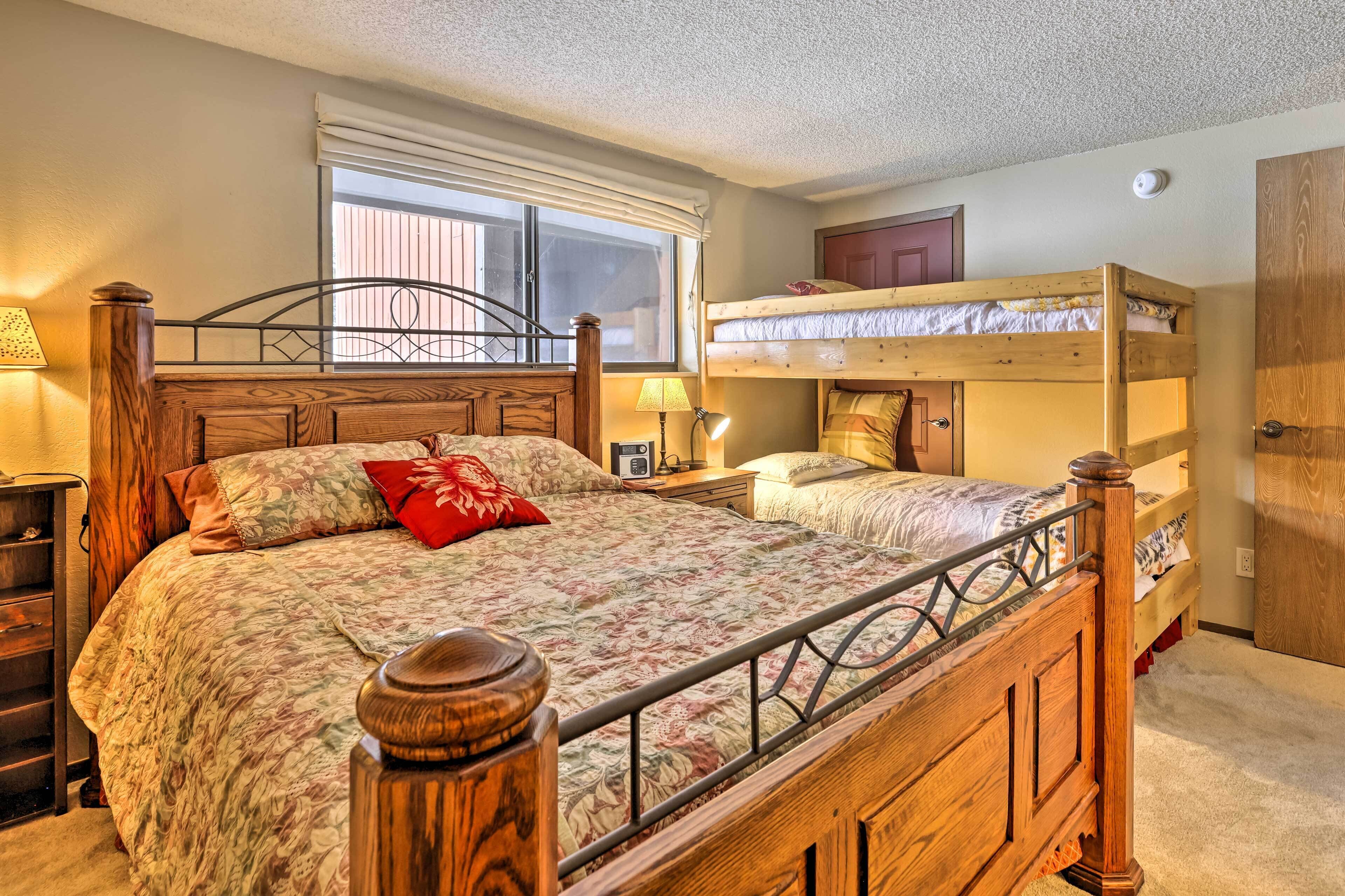 Un dormitorio con una cama de madera, una ventana con persianas, una cama nido y una puerta.