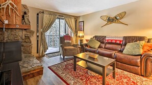 A cozy living room with a stone fireplace, leather sofa, and a large window with curtains. - Gorgeous Winter Park Condo w/ Private Deck! (Winter Park)