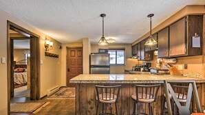 A kitchen with a central island, bar stools, wooden cabinets, stainless steel appliances, and pendant lighting. - Gorgeous Winter Park Condo w/ Private Deck! (Winter Park)