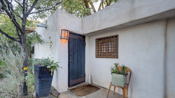 A courtyard with a dark wooden door, a wall-mounted light fixture, a potted plant, and a small bench. - Adobe Studio: 2 Blocks to Dtwn Santa Fe Plaza! (Santa Fe)