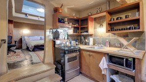 A compact kitchen with a stove, oven, microwave, and wooden shelves. - Adobe Studio: 2 Blocks to Dtwn Santa Fe Plaza! (Santa Fe)