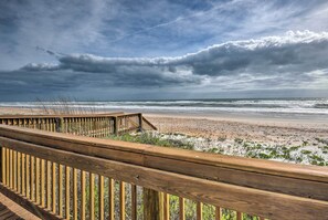 A wooden deck overlooking a beach with a view of the ocean and cloudy sky. - Oceanfront Condo Rental Near Daytona Speedway (Ormond Beach)