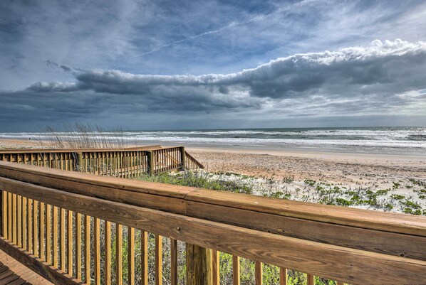 A wooden deck overlooking a beach with a view of the ocean and cloudy sky.
