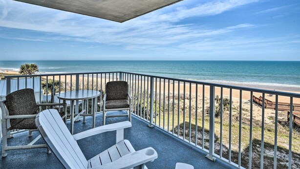 A balcony with two Adirondack chairs, a small round table, and a view of the beach and ocean. - Oceanfront Condo Rental Near Daytona Speedway (Ormond Beach)