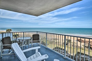 Un balcon avec deux fauteuils Adirondack, une petite table ronde et une vue sur la plage et l’océan.
