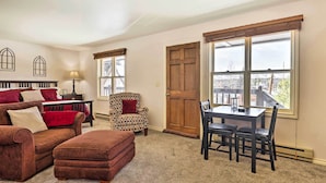 A cozy living room with a brown sofa, matching ottoman, and patterned armchair. A wooden dining table with chairs is positioned near large windows. - 3 Mi to National Park: Cozy Studio in Grand Lake (Grand Lake)