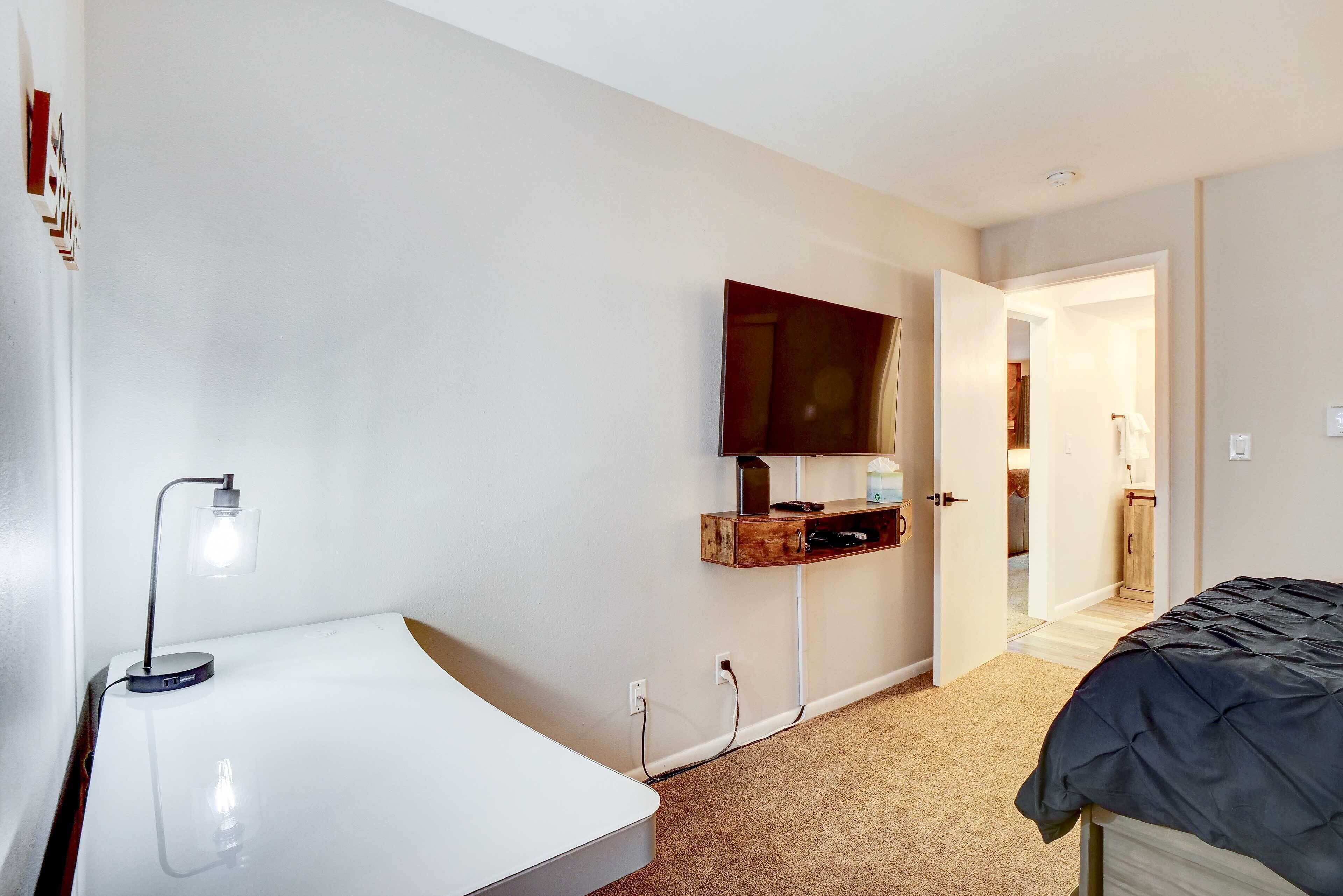 Une chambre à coucher comprenant un lit, une table de chevet avec une lampe, un téléviseur fixé au mur et une étagère en bois avec un miroir.