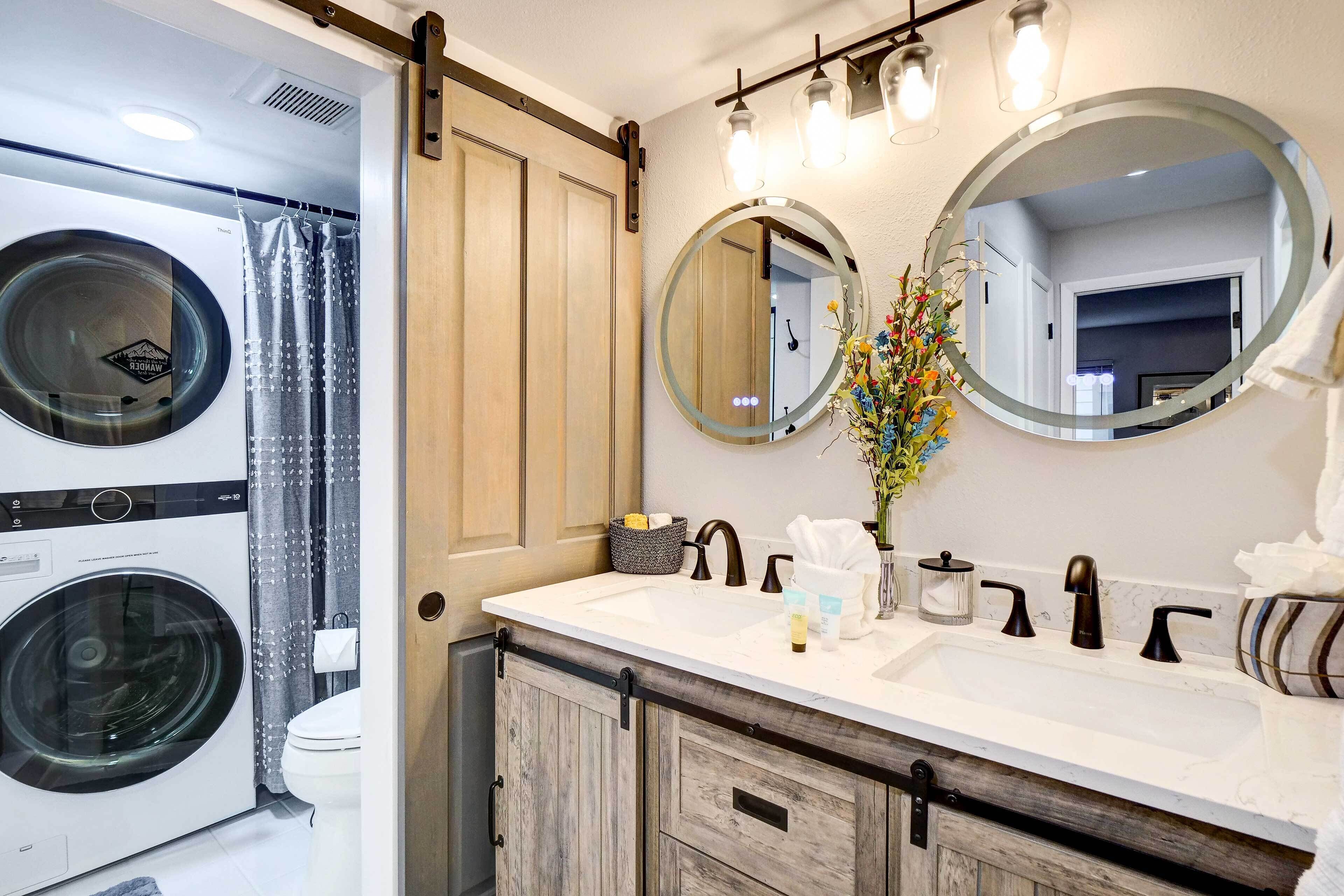 A bathroom with a washing machine, a toilet, a sink with two mirrors, and a shower curtain.