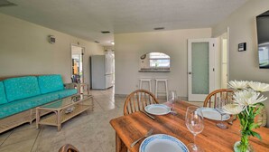 Una sala de estar con un sofá color turquesa, una mesa de comedor de madera dispuesta con platos y copas de vino, y una cocina al fondo.