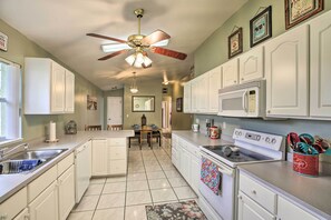 A kitchen with white cabinets, a microwave, a stove, and a ceiling fan. - Lake Okeechobee Fishing Retreat w/ Fire Pit! (Clewiston)