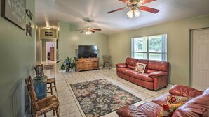 A spacious living room with a red leather couch, a television, and two ceiling fans.