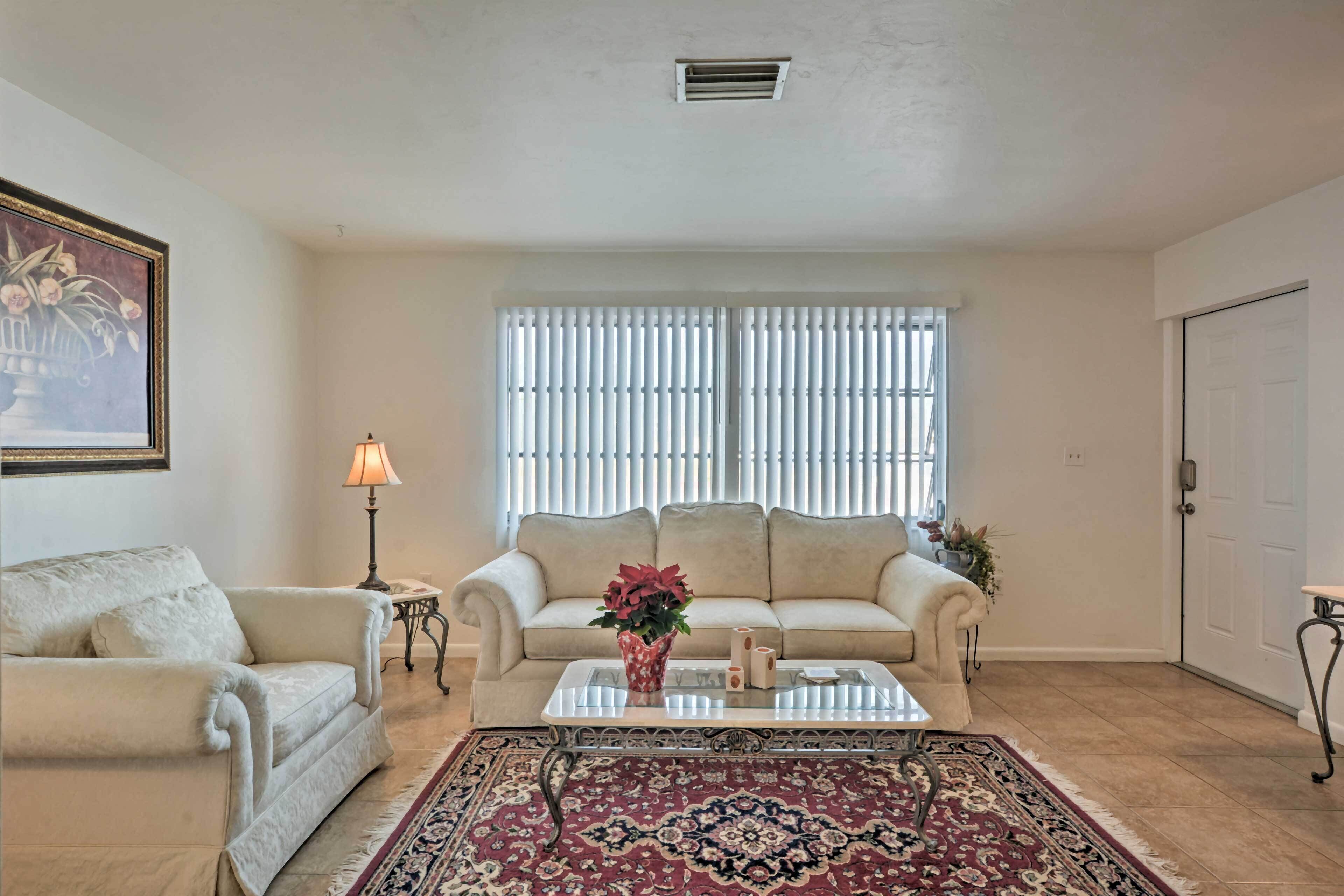 A living room with a beige sofa, a coffee table, a patterned rug, a lamp, and a painting on the wall.