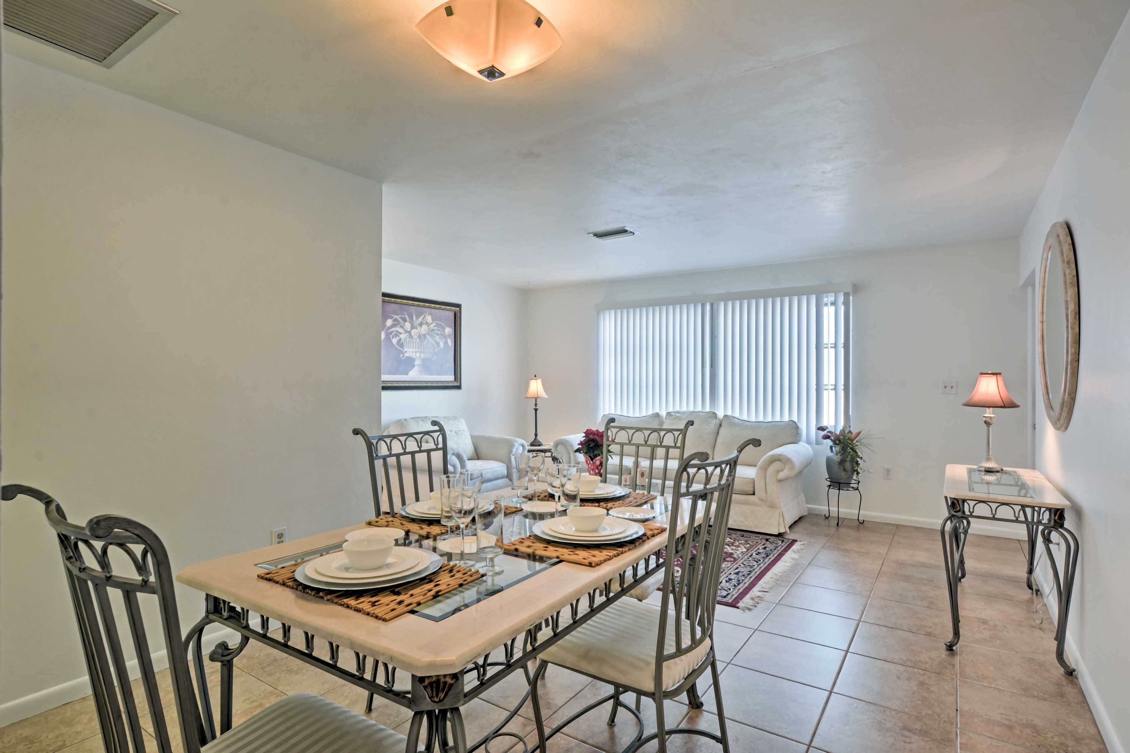 A dining area with a table set for four, surrounded by metal chairs, and a living area with a sofa and a lamp.