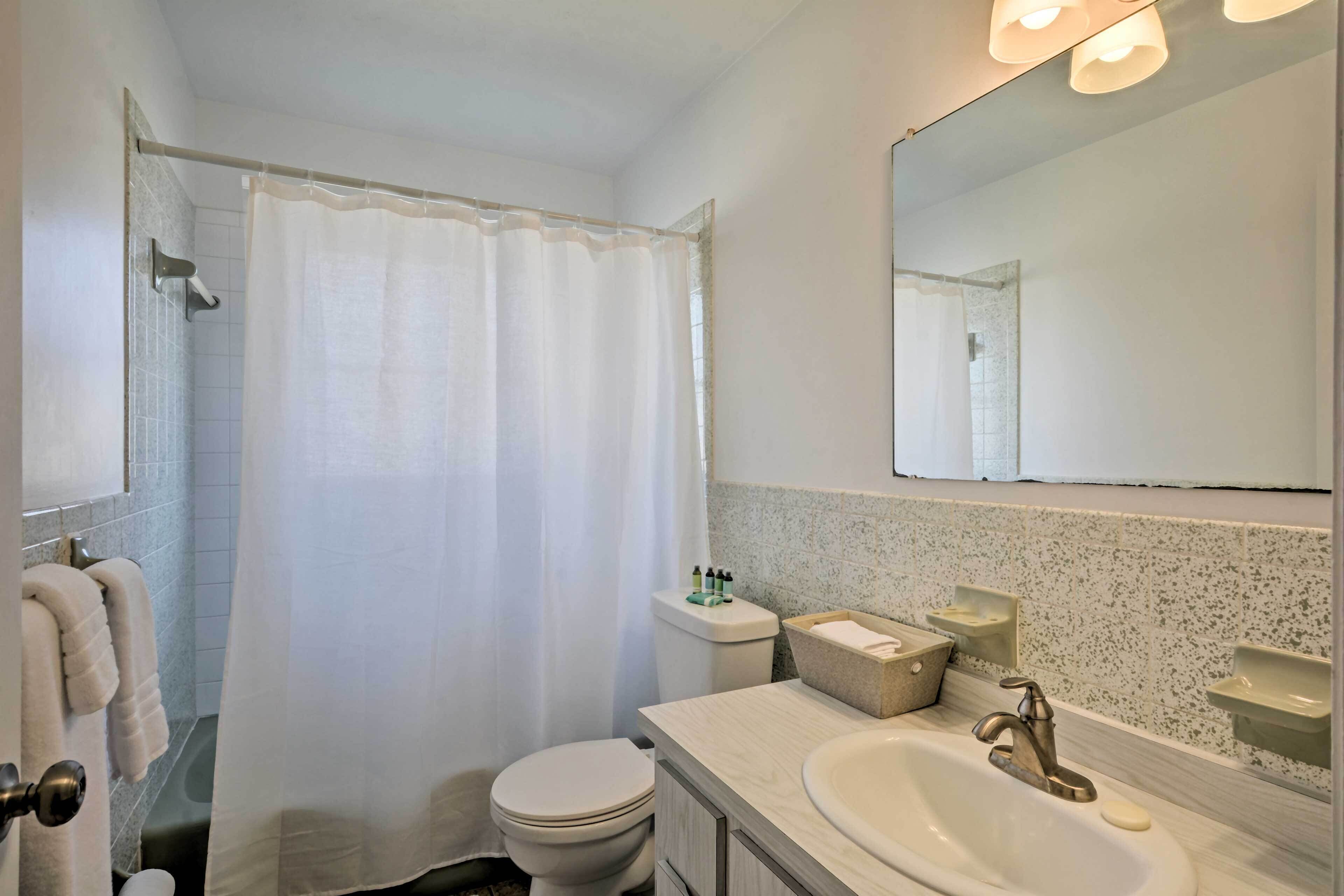 A bathroom with a shower, toilet, sink, and mirror.