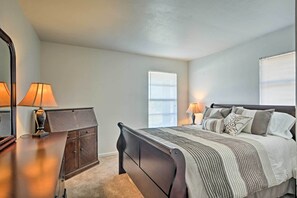 Ein Schlafzimmer mit Bett, Nachttischlampen, einem Schminktisch und einem Fenster mit Jalousien.