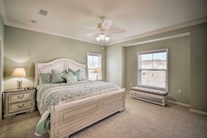 Quarto com cama, mesas de cabeceira, um banquinho e um ventilador de teto.
