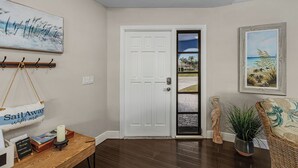 A hallway with a white door, a wooden table with a candle, a sign, and a framed painting. - Canal-front Oasis w/ Dock & Kayaks in Cape Coral! (Cape Coral)