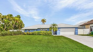 A residential house with a blue exterior, a white garage door, and a well-maintained lawn. - Canal-front Oasis w/ Dock & Kayaks in Cape Coral! (Cape Coral)