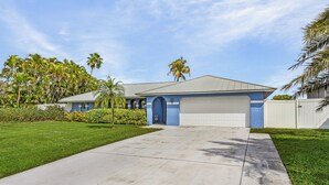 A two-story house with a garage, surrounded by well-maintained lawns and palm trees. - Canal-front Oasis w/ Dock & Kayaks in Cape Coral! (Cape Coral)