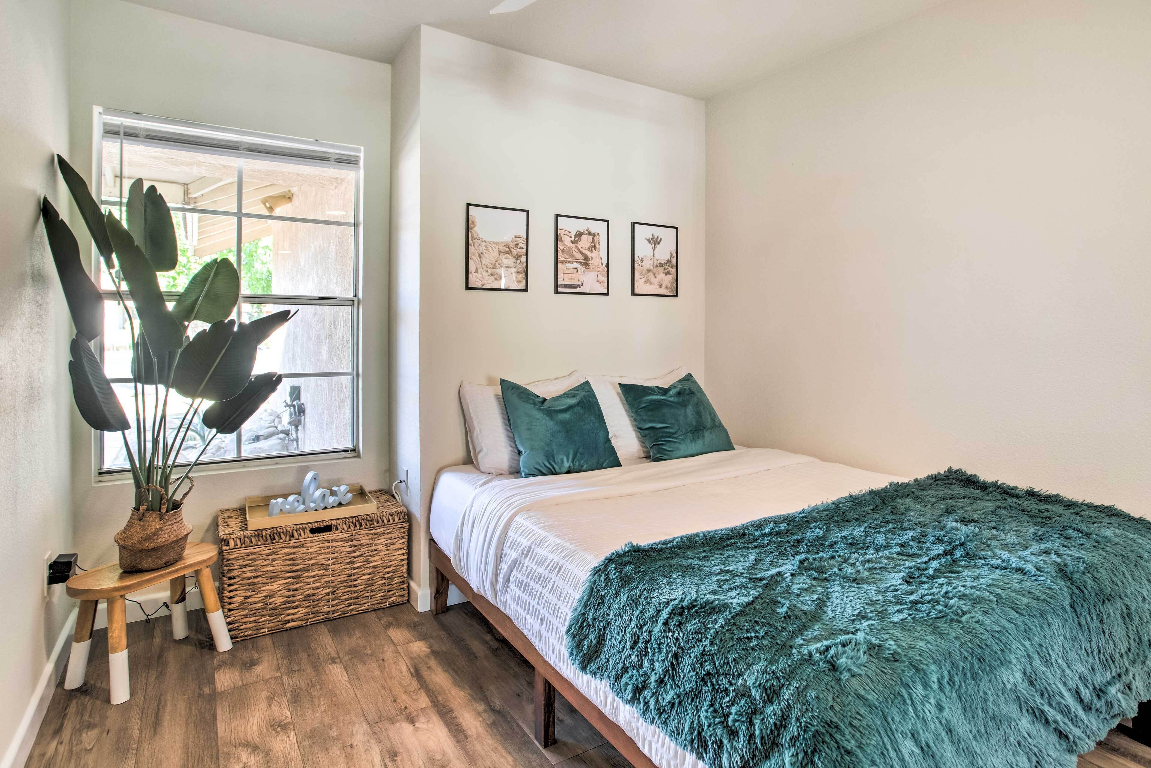 Een slaapkamer met een bed, een raam, een plant en drie ingelijste foto’s aan de muur.