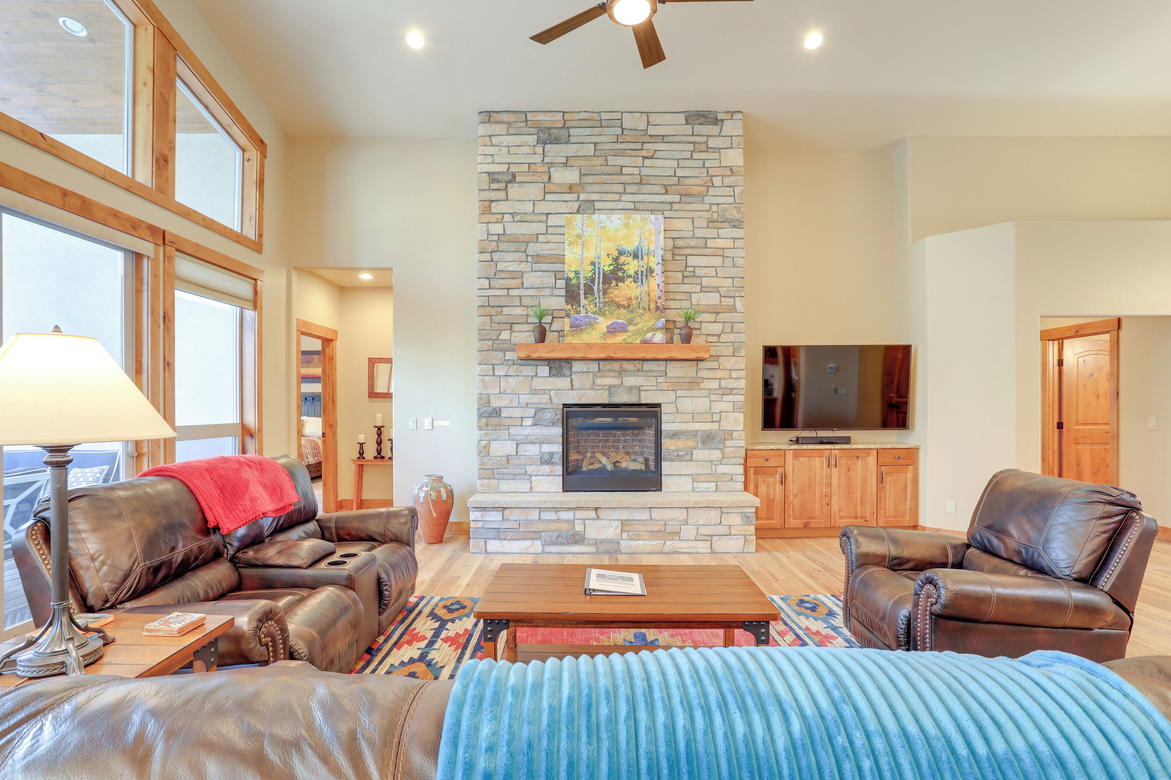 A spacious living room with a stone fireplace, leather furniture, and large windows.