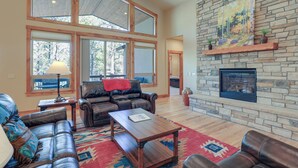 A spacious living room with leather sofas, a wooden coffee table, and a stone fireplace. Large windows allow natural light to fill the space. - Beautiful Pagosa Springs Home w/ Deck & Grill (Pagosa Springs)