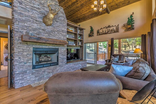 A cozy living room with a stone fireplace, leather furniture, and a large window overlooking a deck.