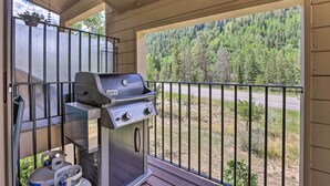 A balcony with a grill and propane tank, overlooking a forested area and a road. - Cozy Vail Condo ~ 4 Mi to Vail Ski Resort! (Vail)