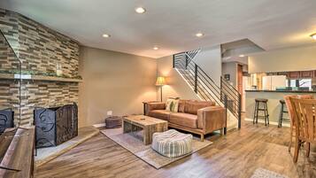 A modern living room with a stone accent wall, a wooden coffee table, a leather sofa, and a staircase leading to a kitchen area.