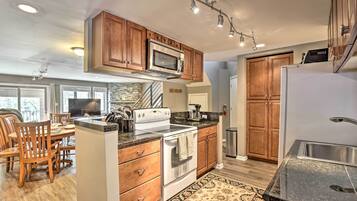 A modern kitchen with wooden cabinets, stainless steel appliances, and a dining area with wooden chairs and a table.