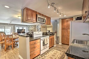 A modern kitchen with wooden cabinets, stainless steel appliances, and a dining area with wooden chairs and a table. - Cozy Vail Condo ~ 4 Mi to Vail Ski Resort! (Vail)