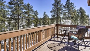 Une terrasse en bois avec une table et des chaises, entourée de grands pins et recouverte de neige.