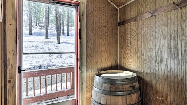 Un intérieur en bois avec une fenêtre donnant sur une forêt enneigée. On peut apercevoir un tonneau en bois.