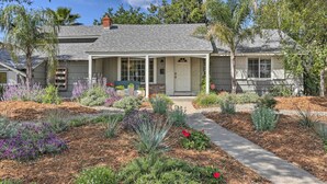 Einbungalow mit einer Veranda, einer Garage und einem gepflegten Garten mit verschiedenen Pflanzen und Blumen.