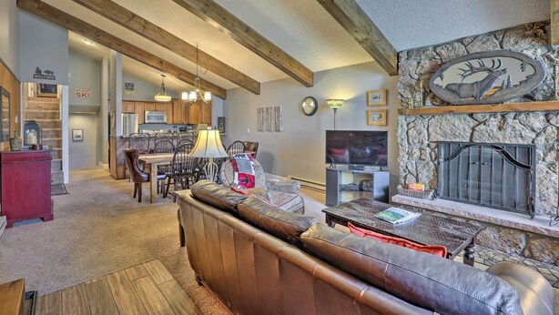 A cozy living room with a fireplace, wooden beams, and a stone wall.