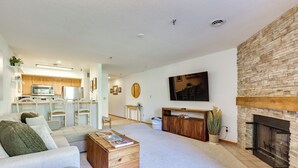A modern living room with a fireplace, a flat-screen TV, and a kitchen in the background. - Walkable Frisco Condo: Mtn Views & Shared Hot Tub! (Frisco)