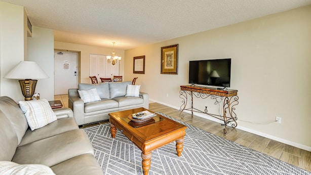 A living room with a sofa, a coffee table, a TV, and a patterned rug. - Beachfront Marco Island Condo w/ Pool Access! (Marco Island)