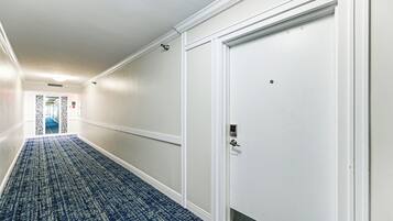 A hallway with a patterned carpet, white walls, and a closed door with a handle.