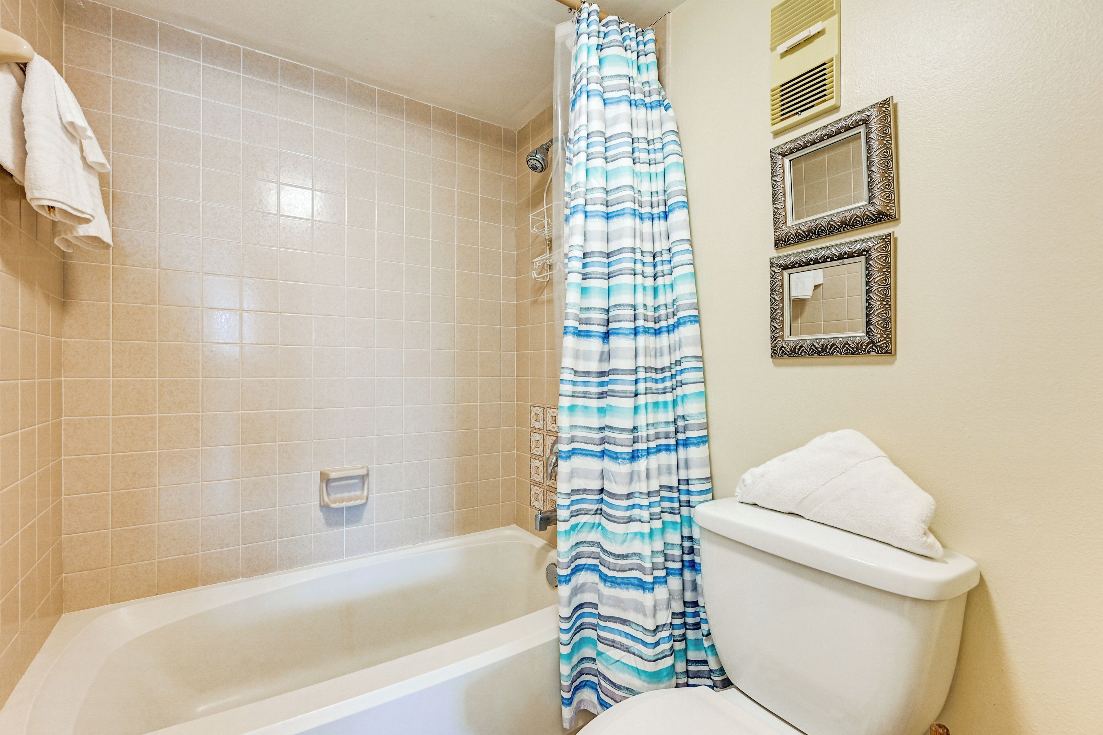 A bathroom with a bathtub, a shower curtain, a toilet, and a wall-mounted towel rack.