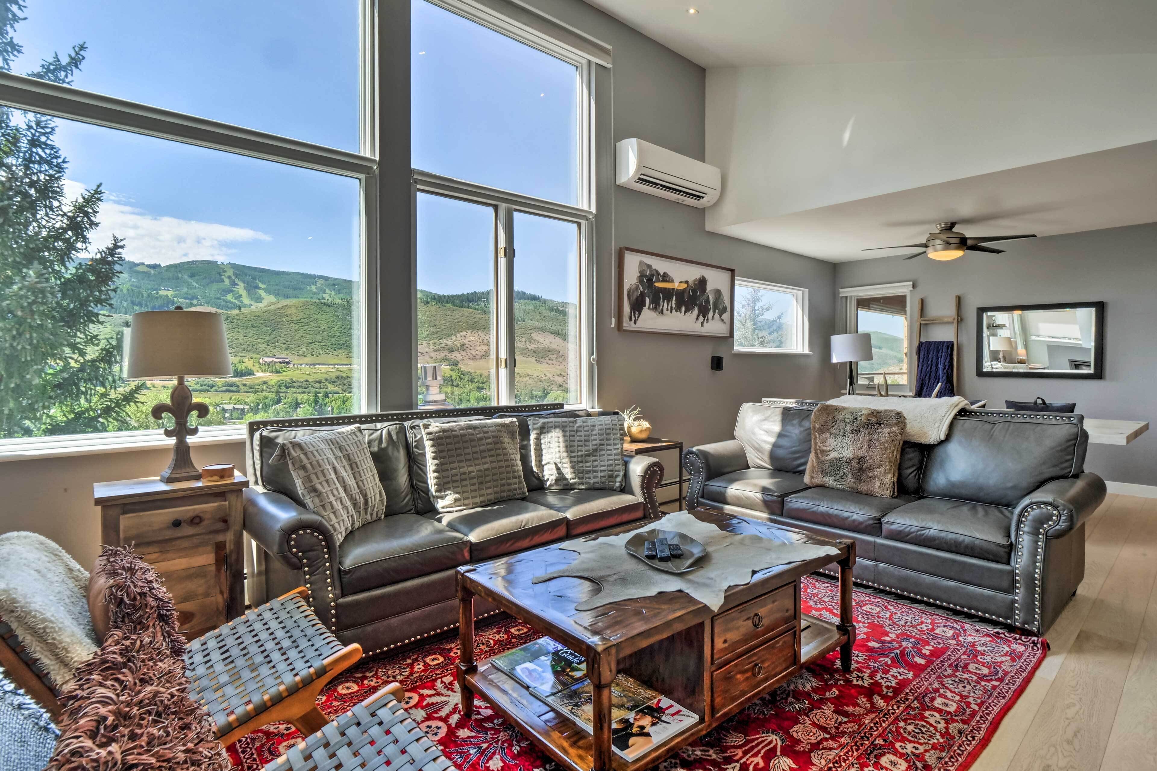 A spacious living room with a large window, leather sofas, a coffee table, and a red patterned rug.