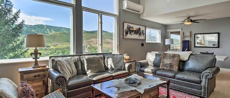 A spacious living room with a large window, leather sofas, a coffee table, and a red patterned rug.