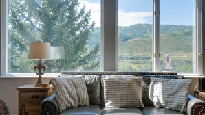 Une pièce avec un canapé en cuir, une lampe et une vue sur une forêt et des collines, visible à travers de grandes fenêtres.