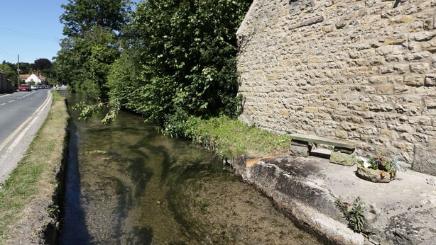 A narrow water channel beside a stone building with a window. - Puddleduck Cottage (Pickering)