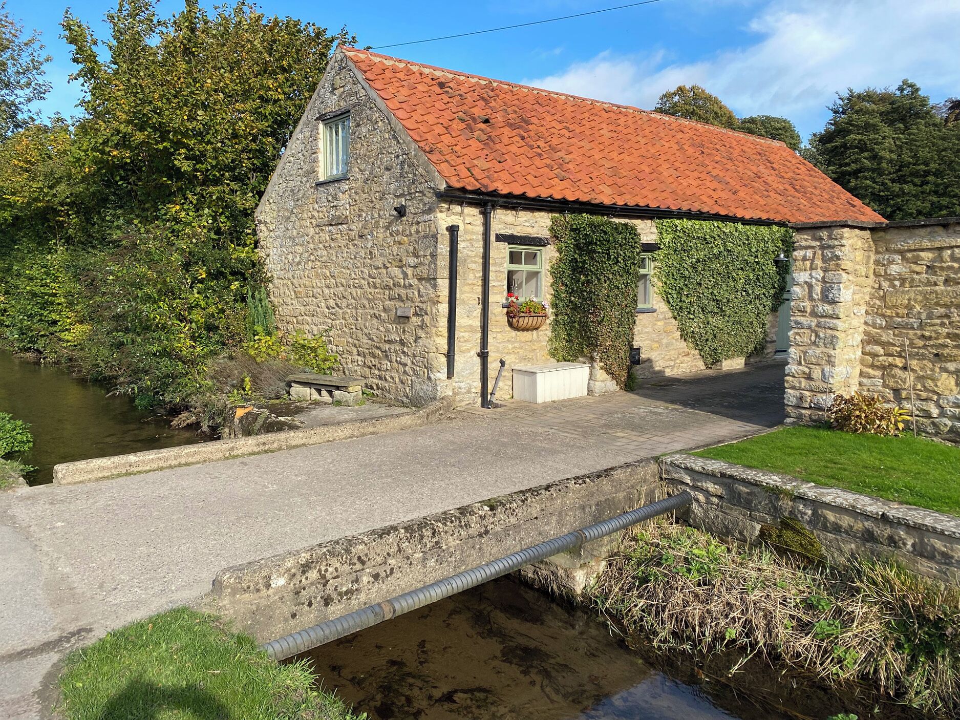 A stone building with a red-tiled roof, a small bridge, and a river.