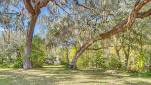 A serene outdoor area with mature trees, a well-maintained lawn, and a small building in the background. - 'laurel on the Lakes' Floral City Escape w/ Canoe! (Floral City)