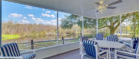 A covered outdoor seating area with white furniture and a view of a lake.