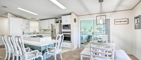 A modern kitchen with white cabinetry, a central island, and a dining area with white chairs.